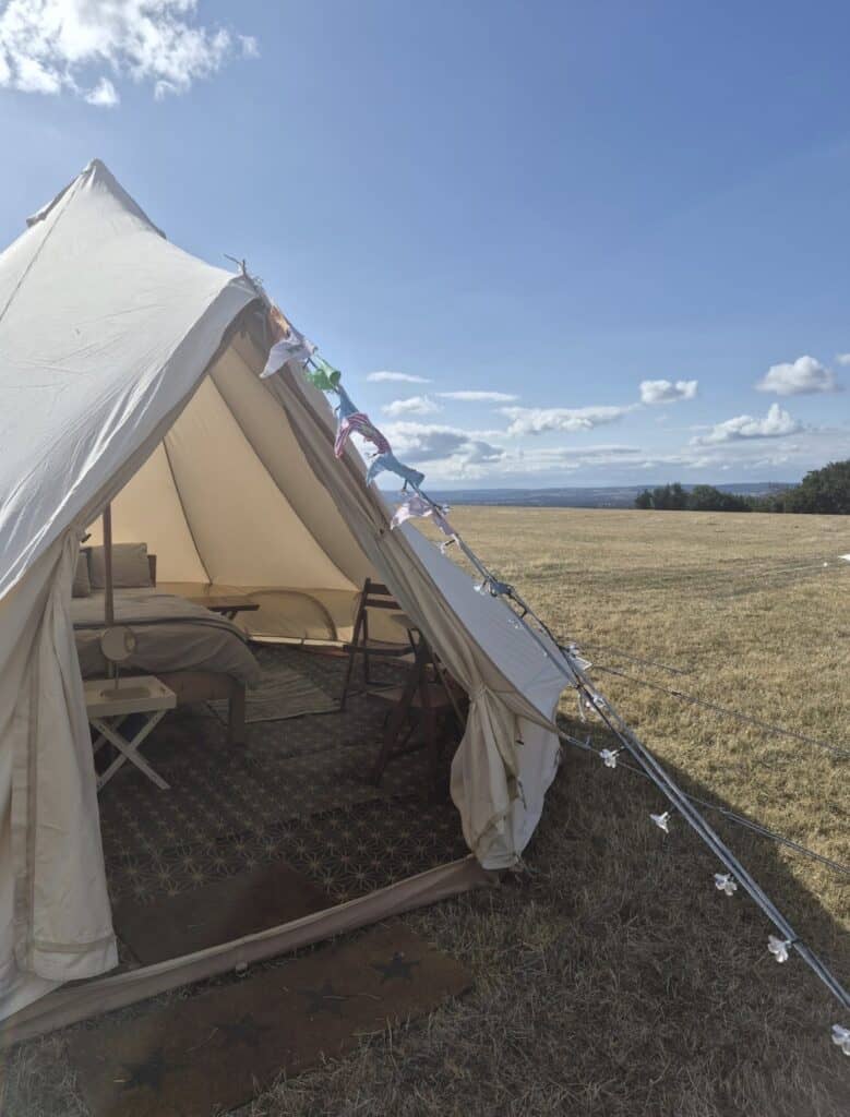 Elegant glamping tent with interior furnishings and scenic countryside view.